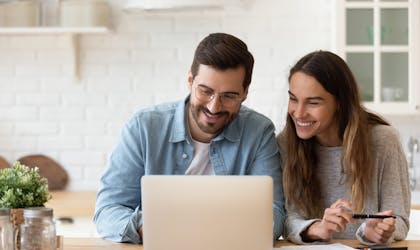 Happy young couple planning budget, reading good news in email, refund or mortgage approval, smiling woman and man looking at laptop screen, checking finances, sitting at table at home together