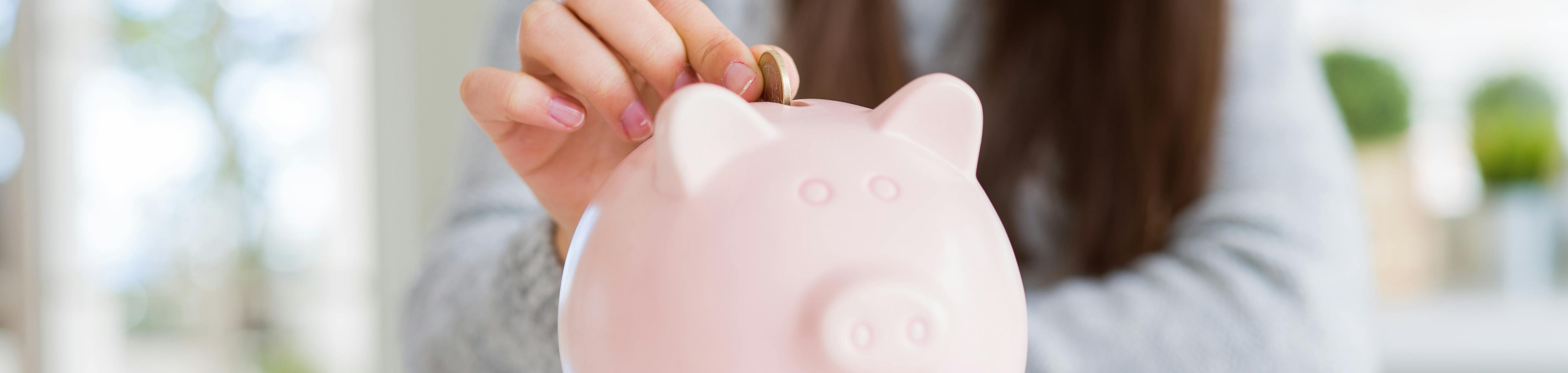 Young woman smiling putting a coin inside piggy bank as savings for investment