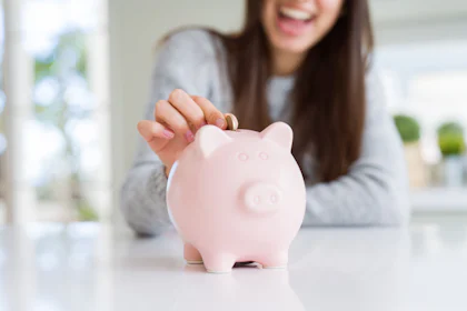 Young woman smiling putting a coin inside piggy bank as savings for investment